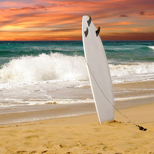 a surfboard standing upright on a sandy beach at sunset